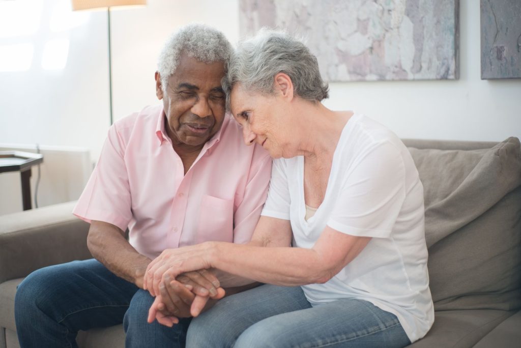 A senior couple lovingly holding hands on a sofa, showcasing affection and support.