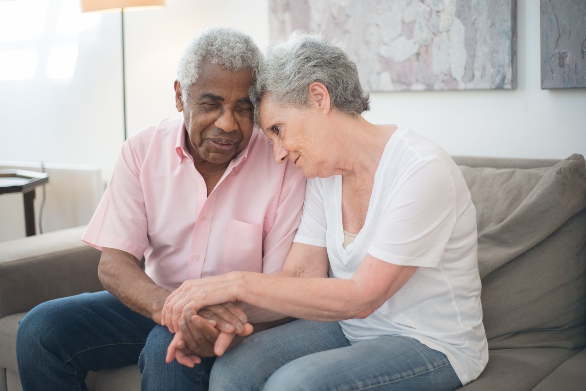 A senior couple lovingly holding hands on a sofa, showcasing affection and support.