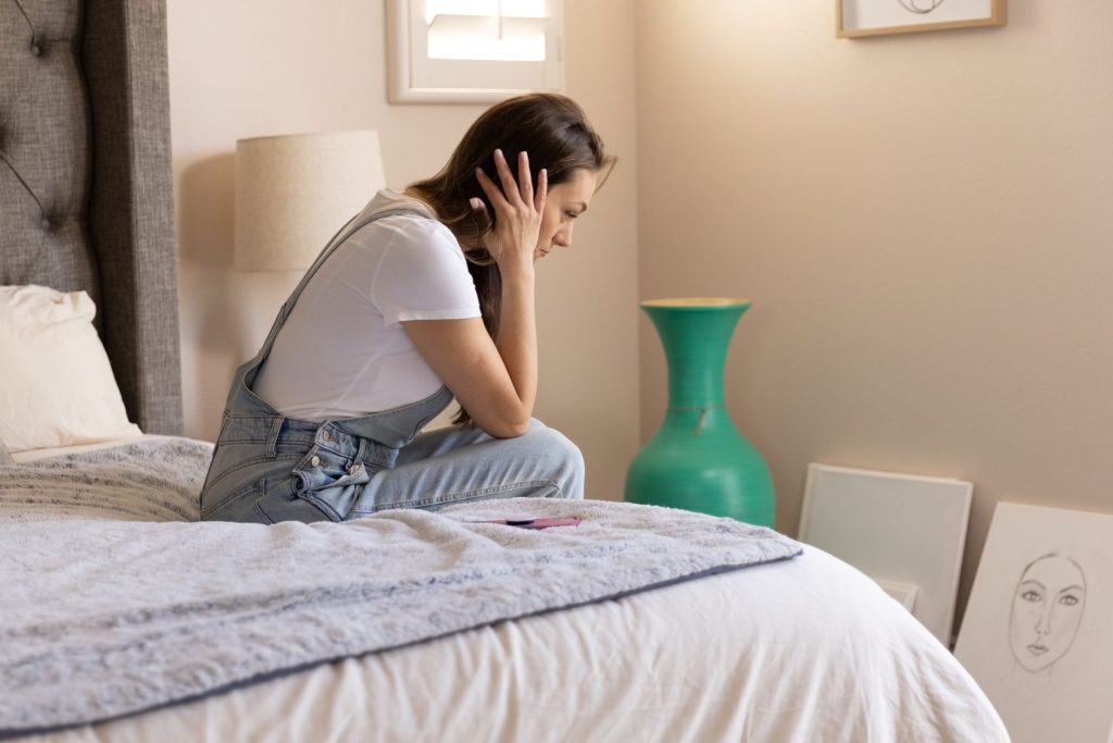 Side view of a woman sitting thoughtfully on a bed in a cozy room, lost in contemplation.