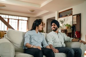 9a5db790 2520 4019 8fcf 2bf730bca2e9 Happy smiling young Indian couple in similar outfits holding hands and looking at each other while resting on sofa in cozy living room