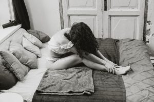 Artistic black and white portrait of a woman sitting on a bed in a contemplative pose.