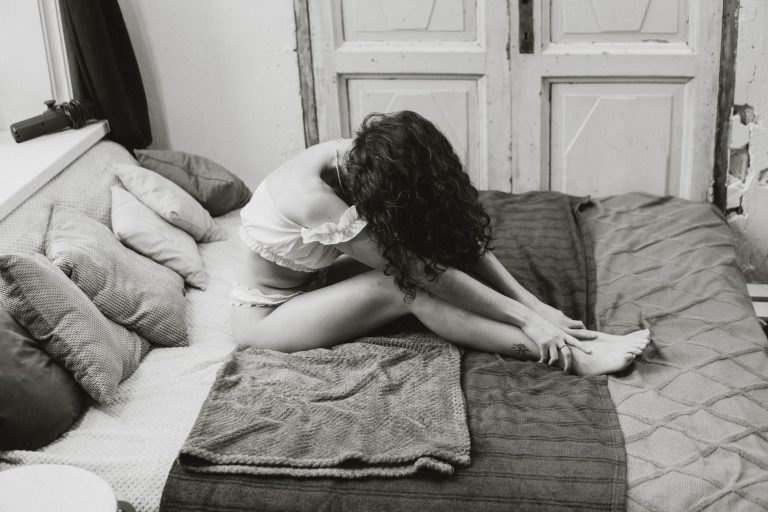 Artistic black and white portrait of a woman sitting on a bed in a contemplative pose.
