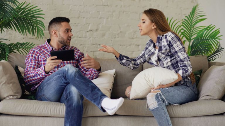 aadd6c9c d9d0 4f8d 9951 f06365f09366 A couple having an argument while sitting on a sofa indoors, showcasing conflict in a relationship.