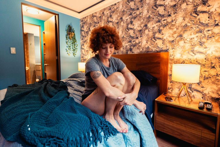 13119cbf 398c 4121 bedb 466bb3286bbe Tattooed woman in a cozy bedroom sitting on a bed, creating a warm and relaxed atmosphere.