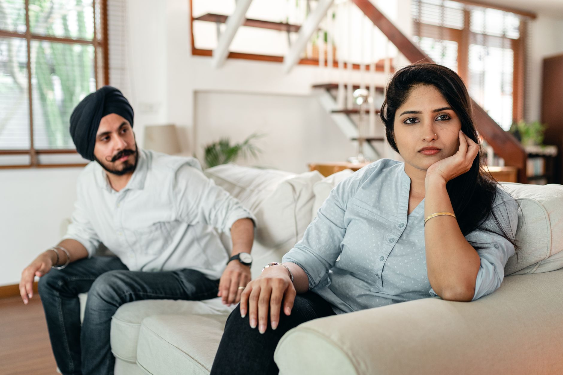 Thoughtful couple sitting on couch in living room at home after quarrel and thinking about reconciliation while looking away pensively