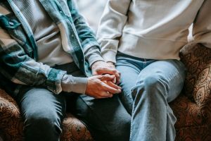 From above of crop anonymous couple in casual clothes holding hands on soft couch