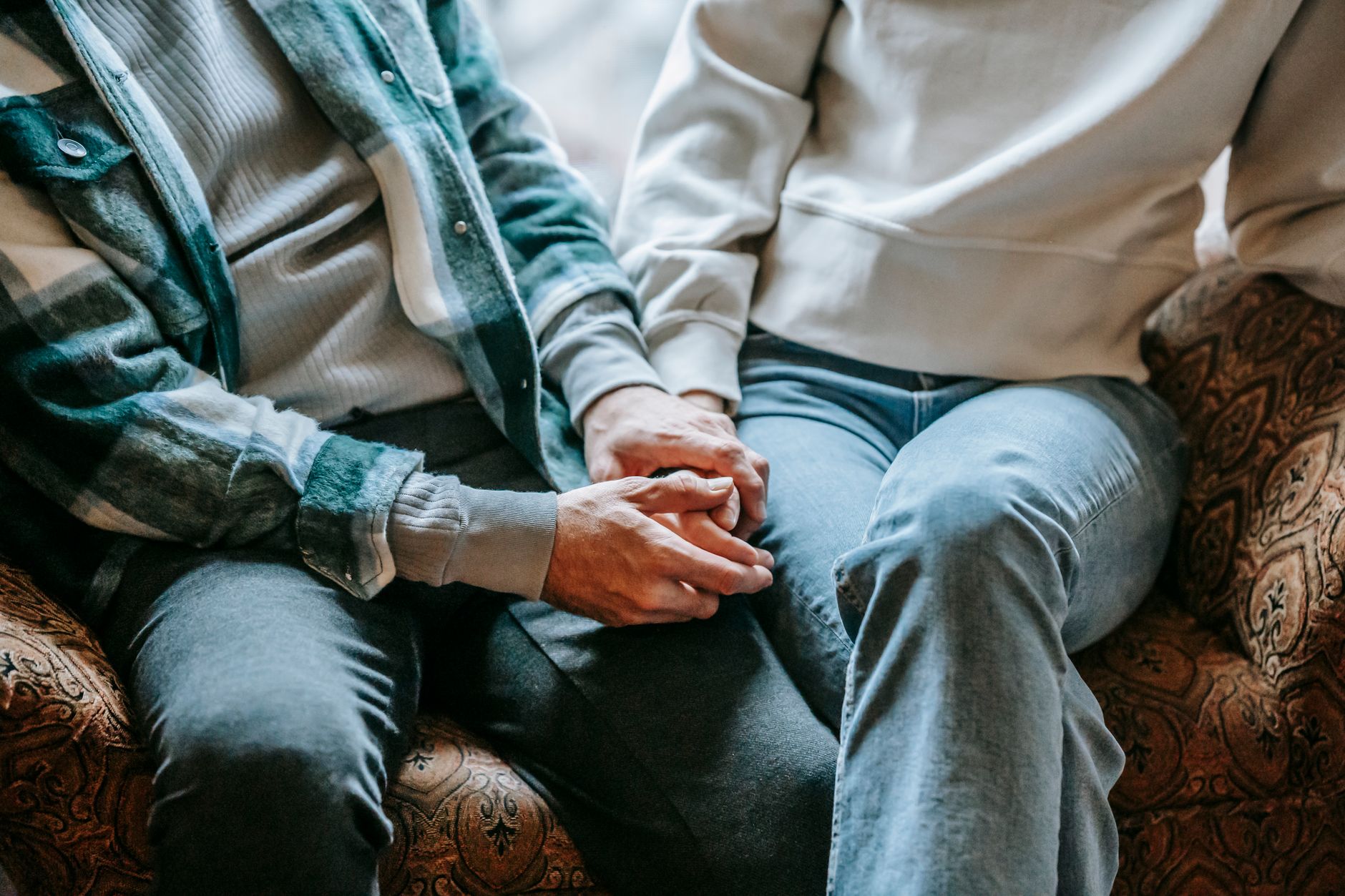 From above of crop anonymous couple in casual clothes holding hands on soft couch