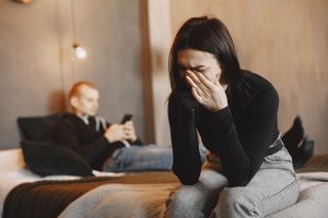 Woman crying on bed, man in background, illustrating relationship stress.