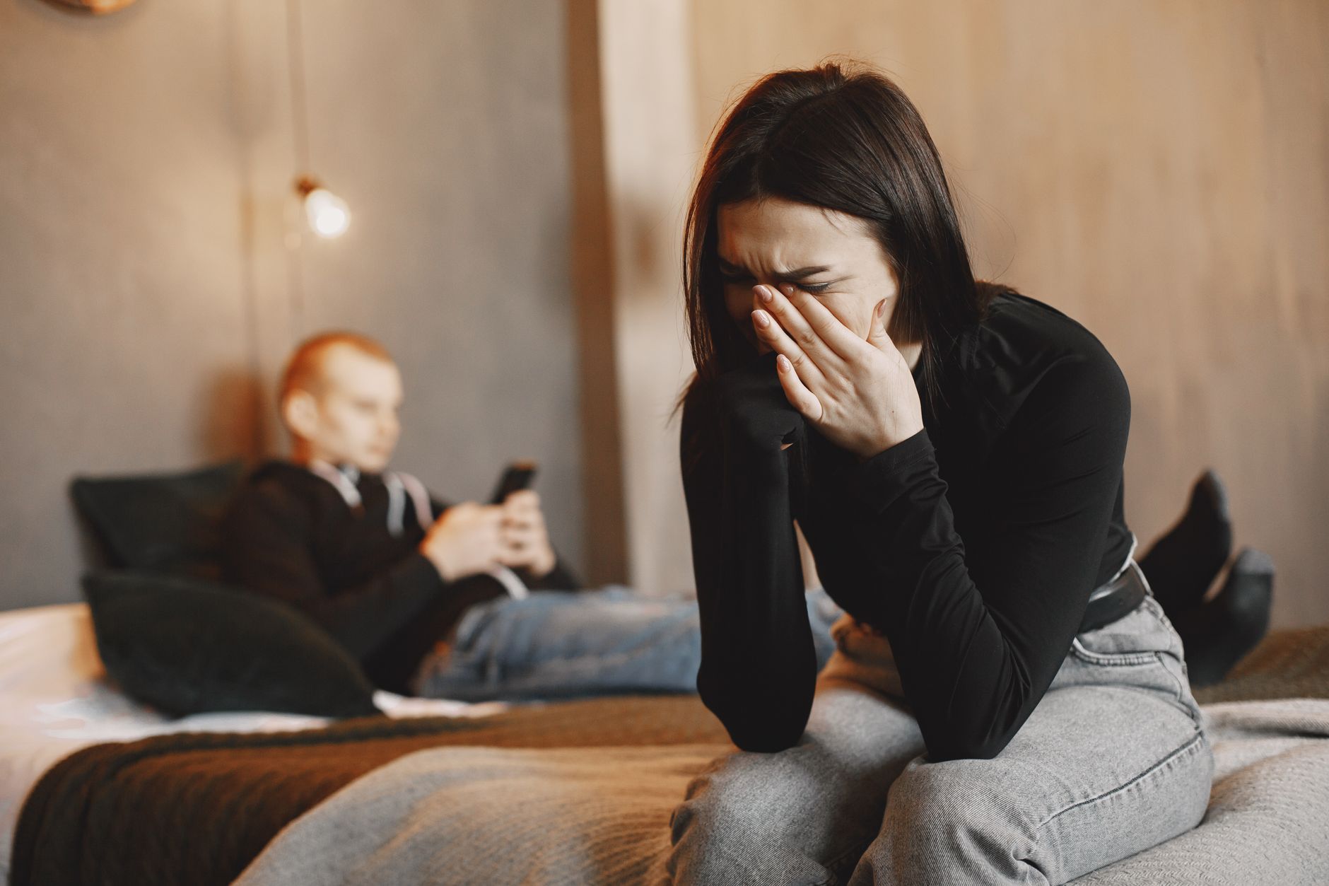 Woman crying on bed, man in background, illustrating relationship stress.