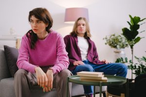 c87ce545 a774 4203 b0a4 f9cb78b2b40e A couple sitting on a sofa with thoughtful expressions, surrounded by home decor.