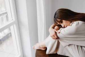 08ab7923 cc64 49dc ab22 a87362cb2011 Thoughtful woman in neutral attire sitting by a window, reflecting emotions.