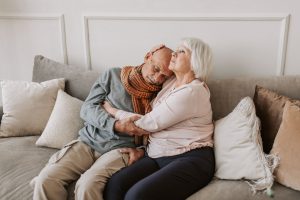 94cabe1e cf6a 46b2 8081 2277225a6077 An affectionate elderly couple sitting together on a comfortable sofa, showing love and care.