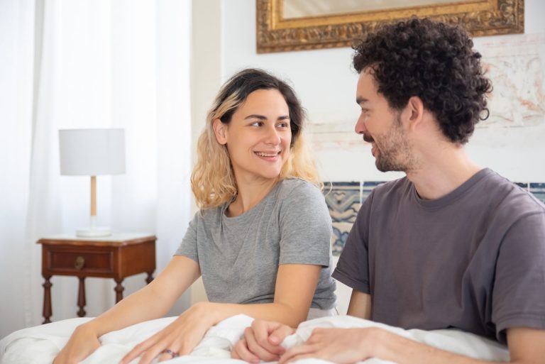 afff2d8e 2a6c 4d4e 82a4 83213d27f4c4 Smiling couple sitting on bed in a bright bedroom with stylish decor.