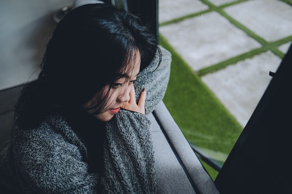 A young Asian woman in a gray sweater gazes pensively out a window in Indonesia.