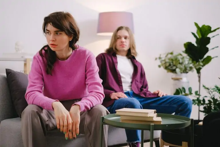 c87ce545 a774 4203 b0a4 f9cb78b2b40e A couple sitting on a sofa with thoughtful expressions, surrounded by home decor.